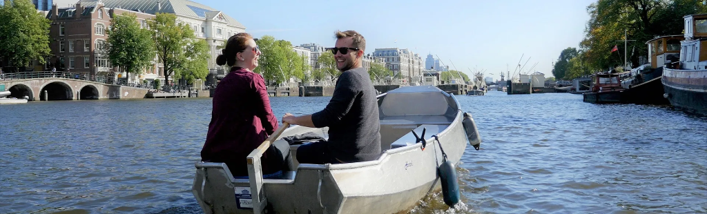 Couple driving a small aluminum self-drive rental boat on Amsterdam canals
