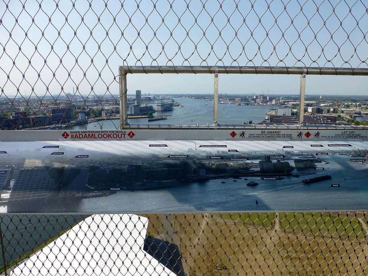 View north-west from the A'DAM Lookout deck through its safety mesh, over the IJ toward Westerdok and the Houthavens
