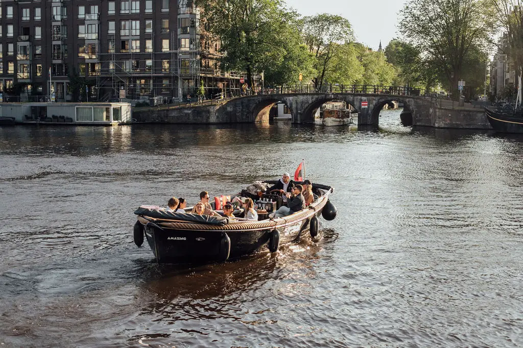 Small open canal boat cruising through central Amsterdam, suitable for bringing a dog