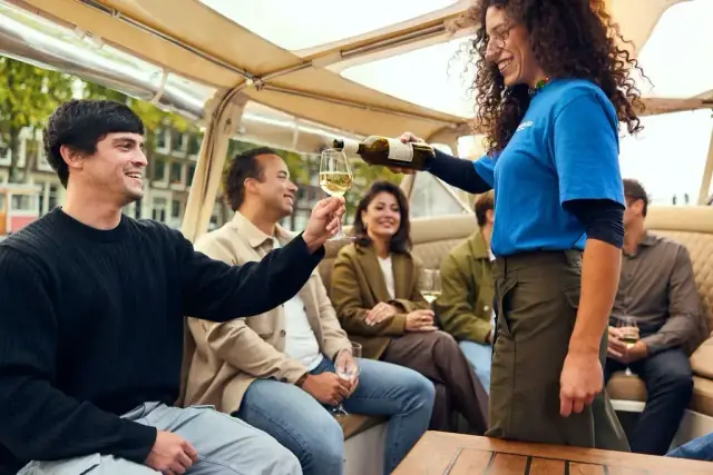 A host in a blue shirt pours wine for guests seated in a covered Starboard boat