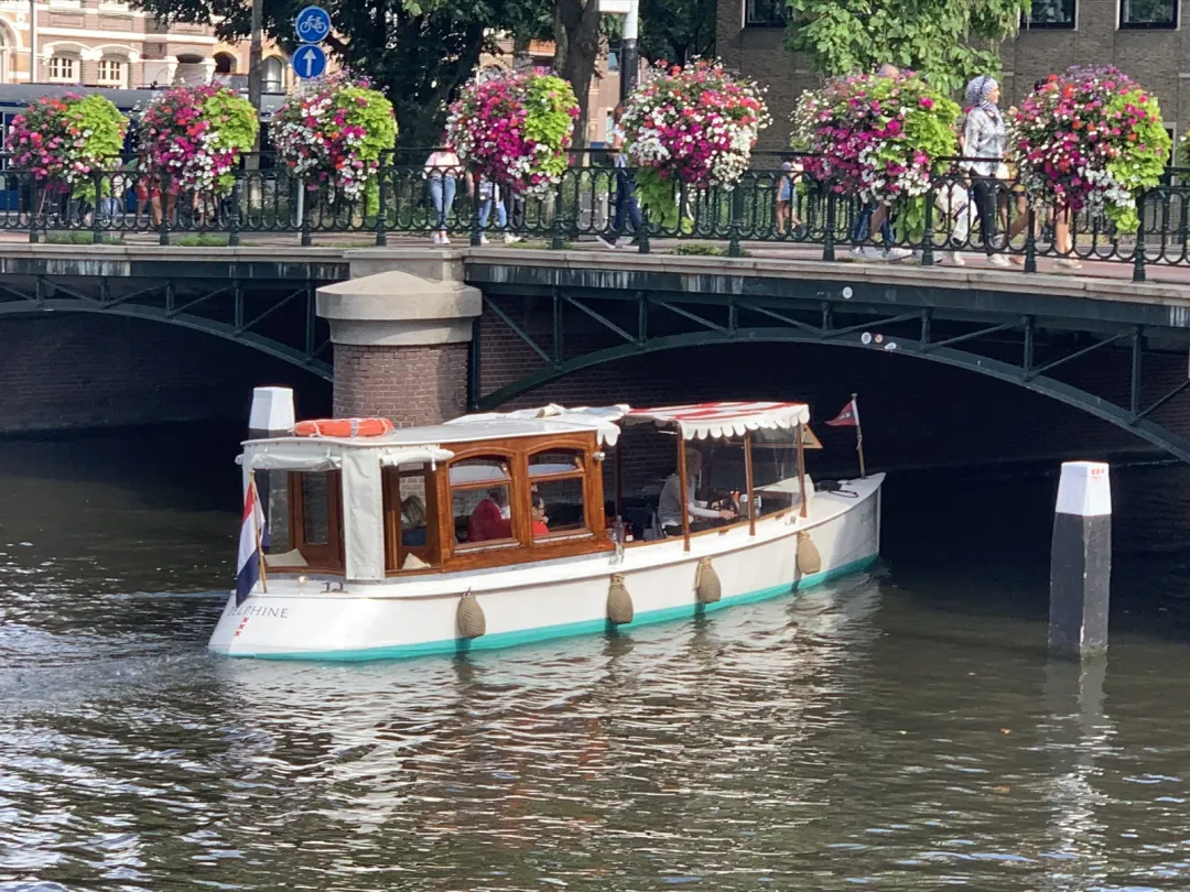Delphine canal boat passing under a bridge hung with flower baskets in Amsterdam