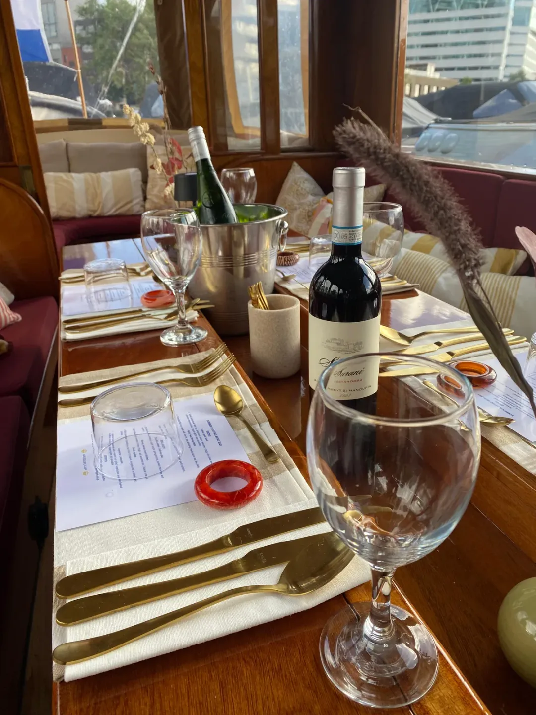 Close view of a boat dining table with a menu card, wine bottle, glass and gold cutlery
