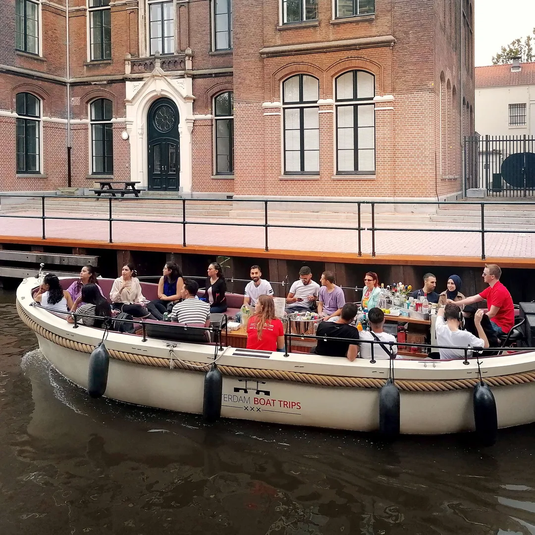 Open white electric canal boat with guests seated along both sides on an Amsterdam canal in daylight