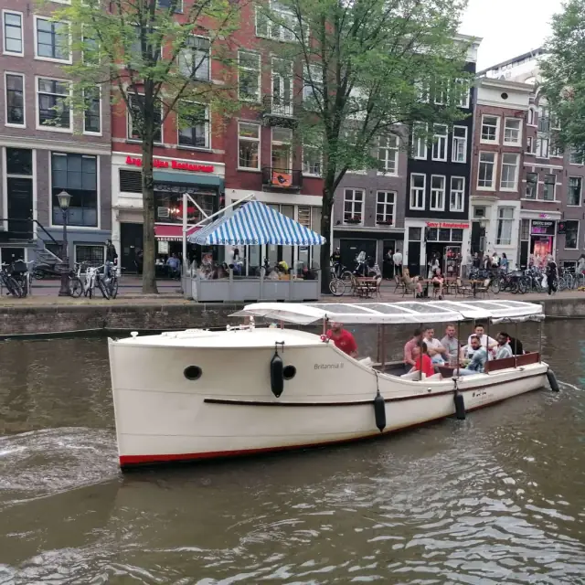 White canal boat with a black bow stripe passing canal houses in Amsterdam