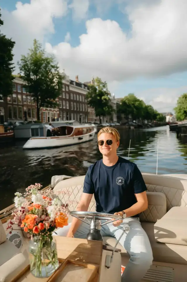 Captain at the helm of an open boat, with a bouquet of flowers on the table beside him