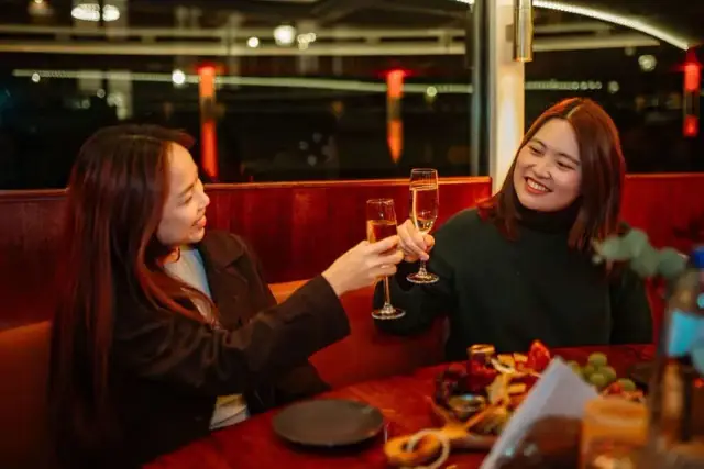 Two guests clink glasses in a leather booth with a platter on the table