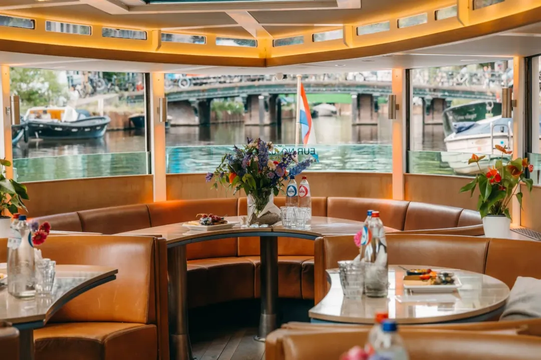 Leather booth seating and round tables on Stan Huygens with canal views through the windows