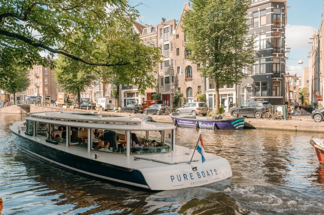 Pure Boats canal boat Stan Huygens cruising an Amsterdam canal in daylight, with a guest at the back