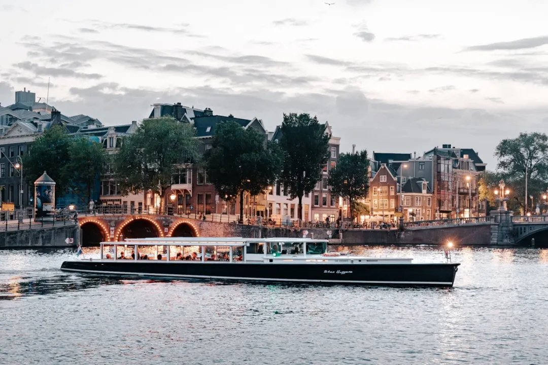 Stan Huygens, a dark-hulled glass-roofed canal boat, on the Amstel at dusk
