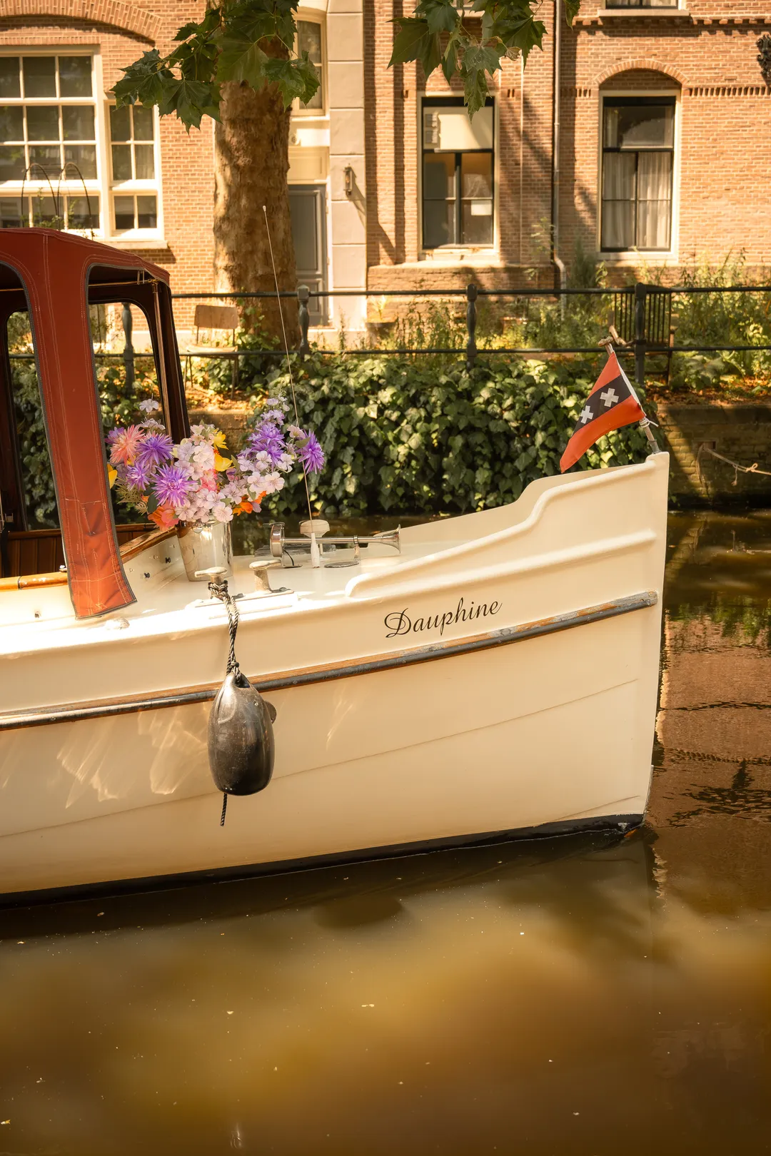 Bow of the salon boat Dauphine with a flower arrangement on deck and the Amsterdam flag