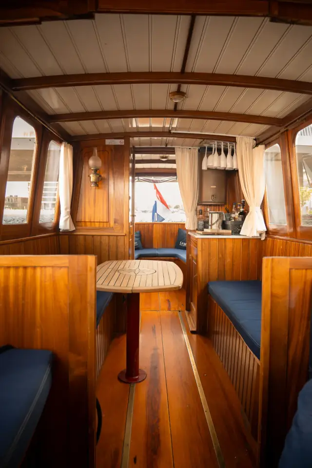 Wood-panelled salon with navy bench cushions, a small table and cream curtains aboard the 1910 boat
