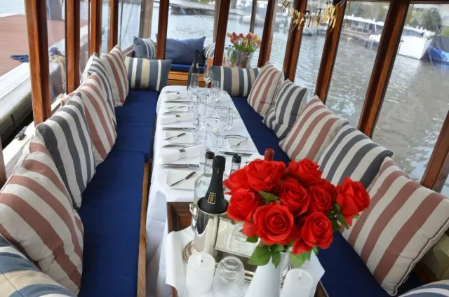 Dinner table laid with red roses, candles and glasses between striped cushions inside the salon of Energie