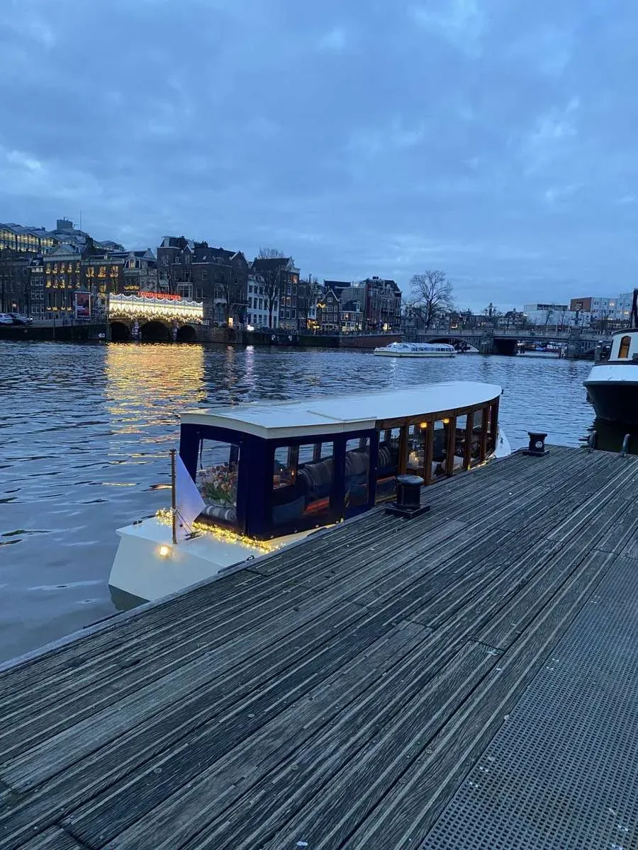 Salon boat Energie with lit windows moored at a wooden pier on the Amstel at dusk