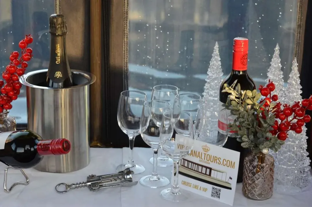 Champagne cooler, wine bottle and glasses on a table inside the salon, with small glittering trees by the window