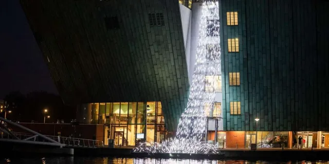 Light artwork of cascading white lights falling beside the green NEMO building in Amsterdam at night