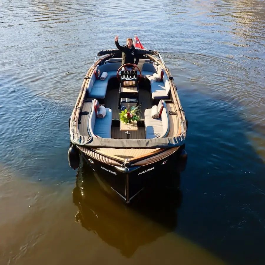 Open electric canal boat seen from above, with cushioned seating and the captain standing at the helm