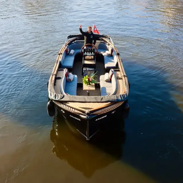 Open electric canal boat seen from above, with cushioned seating and the captain standing at the helm