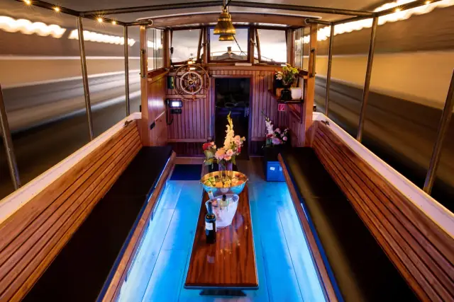 Inside Giuliana in the evening: wooden benches, a table with flowers and wine, and blue lights along the floor