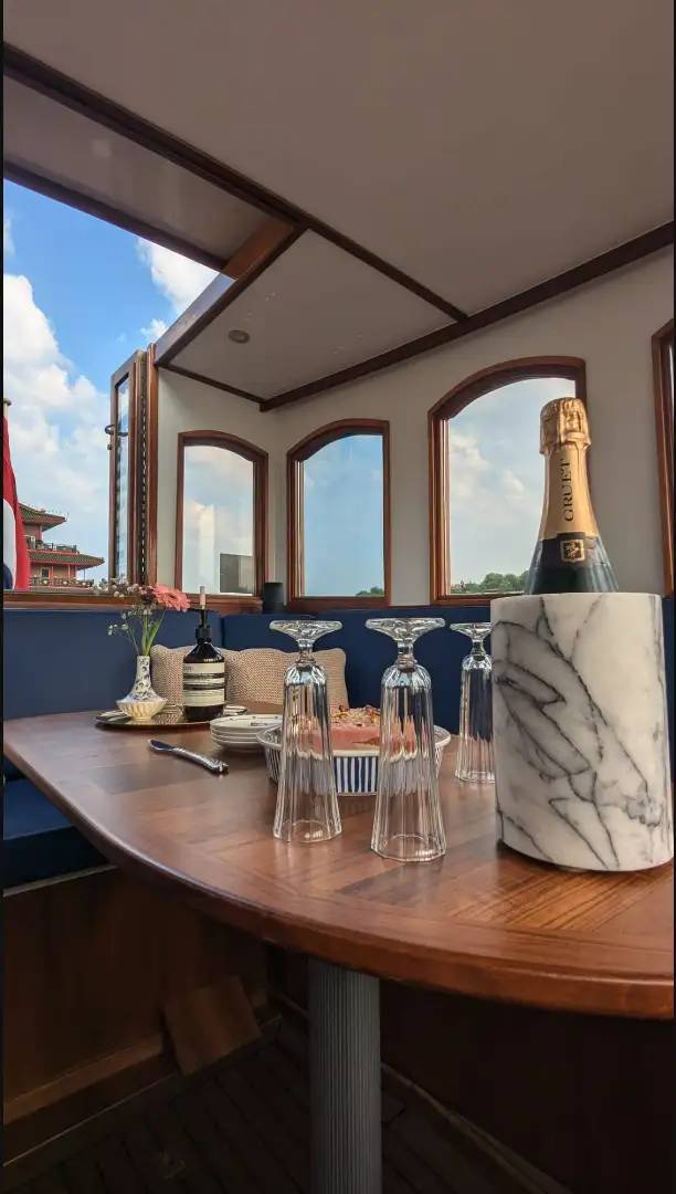 Wooden boat saloon table with champagne in marble cooler, upturned glasses, flowers and arched windows