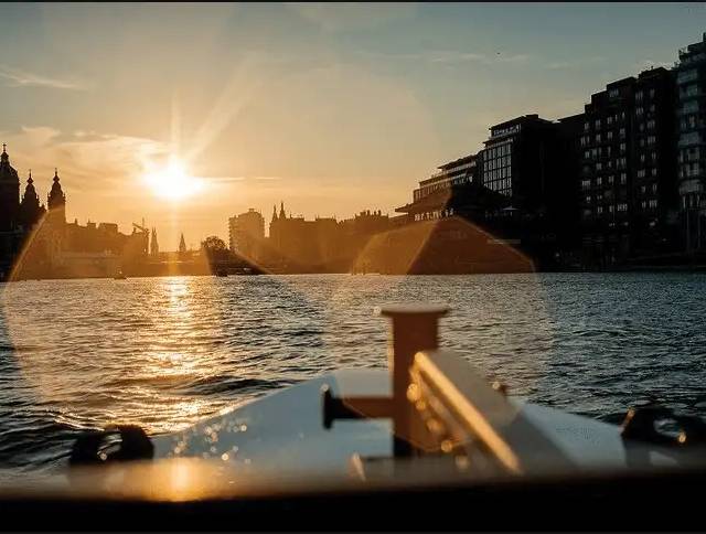Sun setting over Amsterdam's IJ waterfront, seen past a boat's white bow and railing