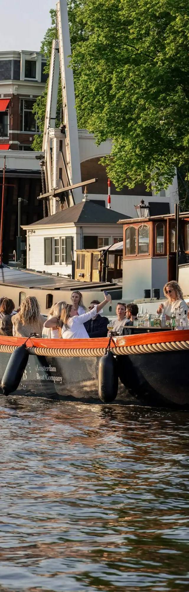 Guests in white taking a selfie aboard an open boat on an Amsterdam canal beside a drawbridge